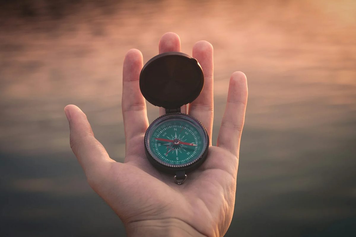 a hand holding a compass pointing west