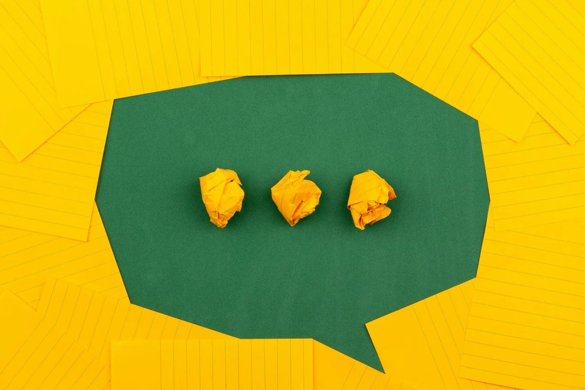 crumpled yellow paper notes arranged as a speech bubble on a green surface